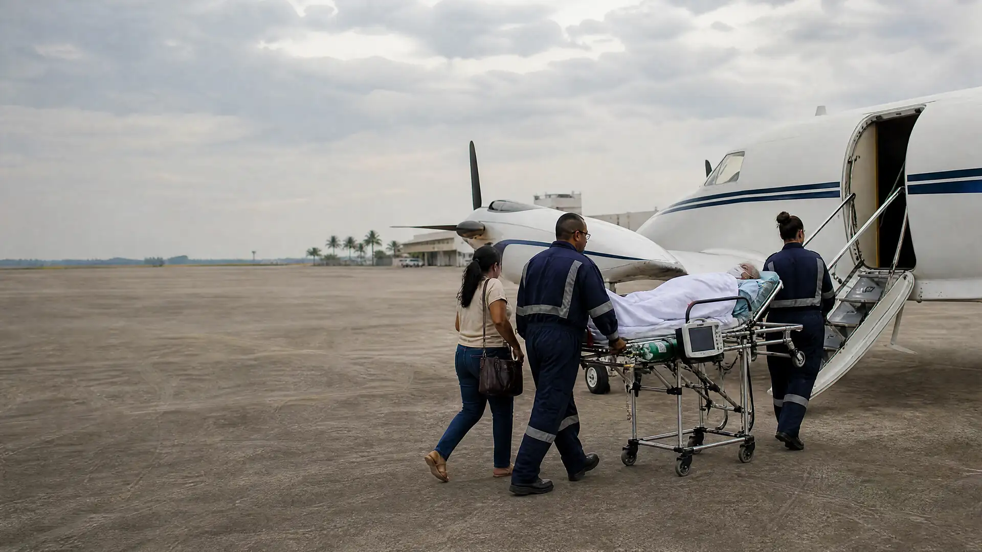 Equipe médica conduzindo um paciente em maca de UTI até uma aeronave ao entardecer
